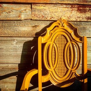 Empty antique wooden chair sitting up against wood slat wall, during golden hour.
